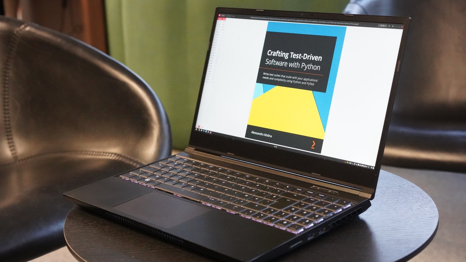 A close-up of a laptop on a table, displaying a book on test-driven software with Python, set in a comfortable environment.